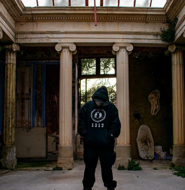 Person standing in an abandoned house wearing a Vandal Wisdom 1312 hoodie